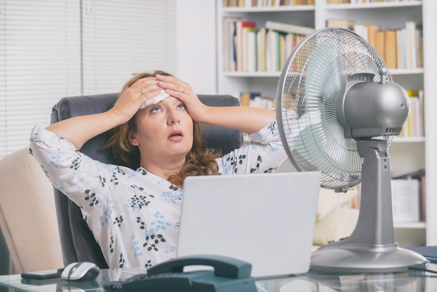 Woman suffers from heat while working in the office and tries to cool off by the fan.