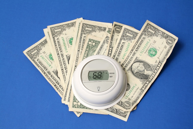 Thermostat sitting on dollar bills with blue background.