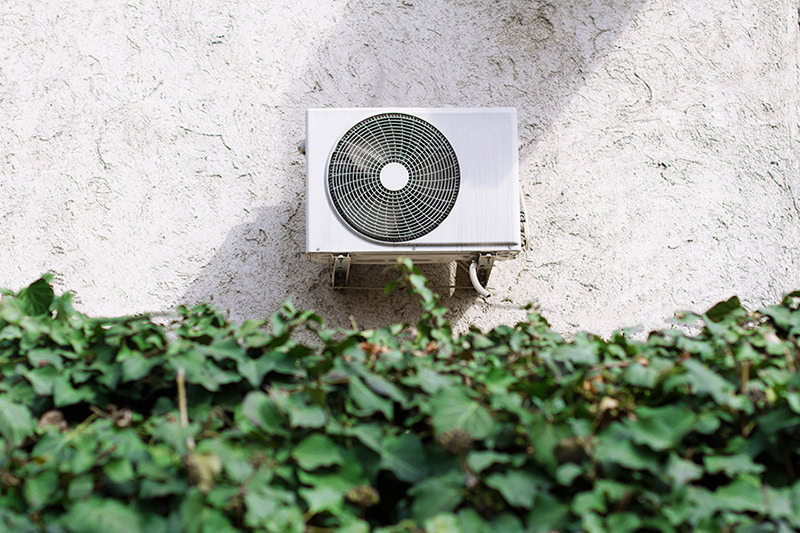 horizontal front view of a white air conditioning unit behind a decorative garden wall of green leaves.