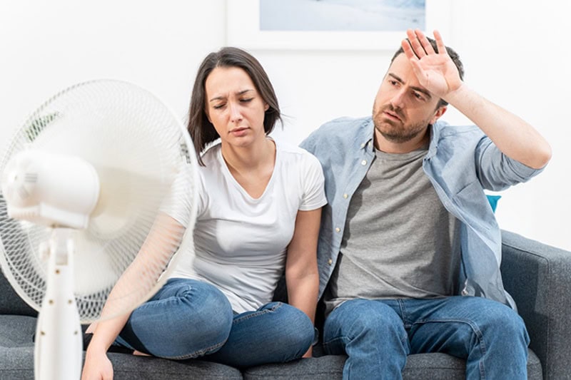 Why Is My AC Blowing Hot Air? Couple trying to refresh during summer heat wave.