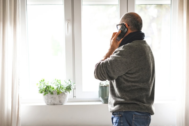 Why Won’t My Furnace Stop Running? Photo of a man on the phone, looking out his window seemingly concerned.