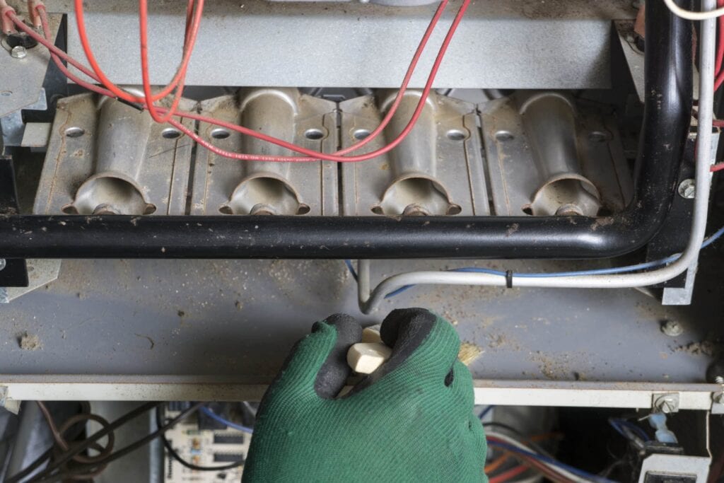 Technician cleaning a burner area of a natural gas furnace.|