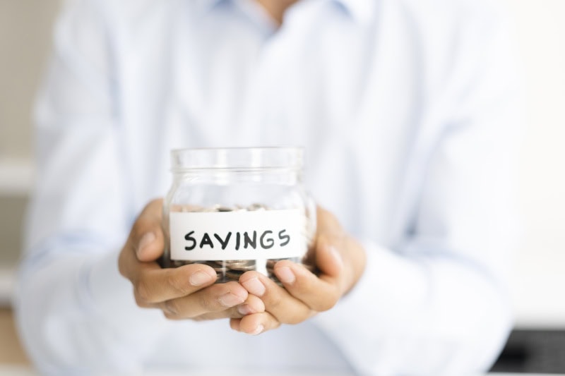 Why Buying a Heat Pump Instead of a Furnace Makes Sense. Photo of a person holding a jar full of coins labeled "Savings".