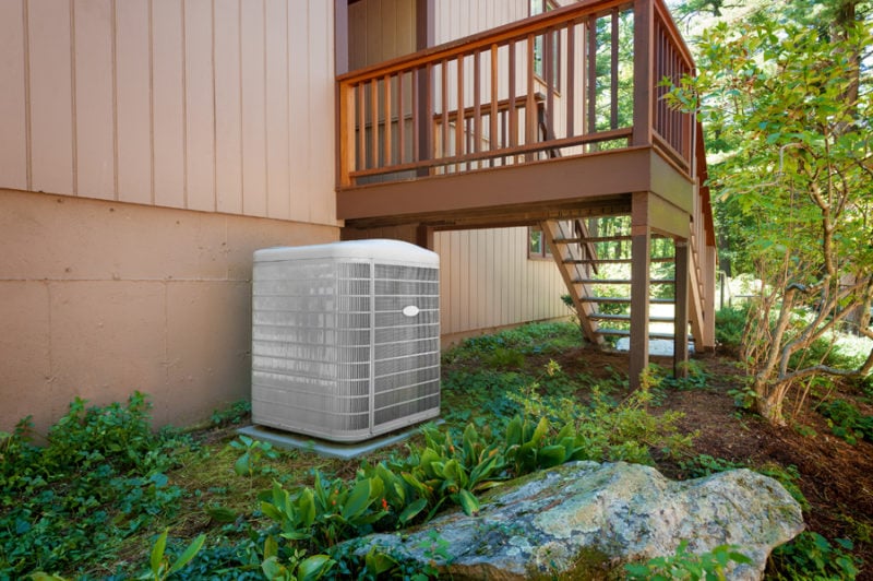 A residential heat pump central air conditioning and heating unit sitting outside a home.|A residential heat pump central air conditioning and heating unit sitting outside a home.