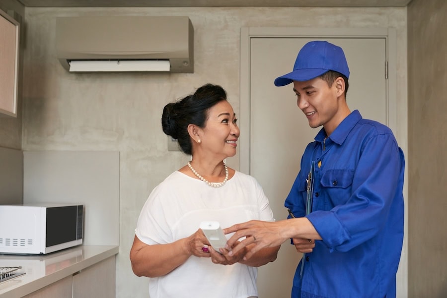 SmiIing technicial explaining Vietnamese senior woman how to use air conditioner remote control.