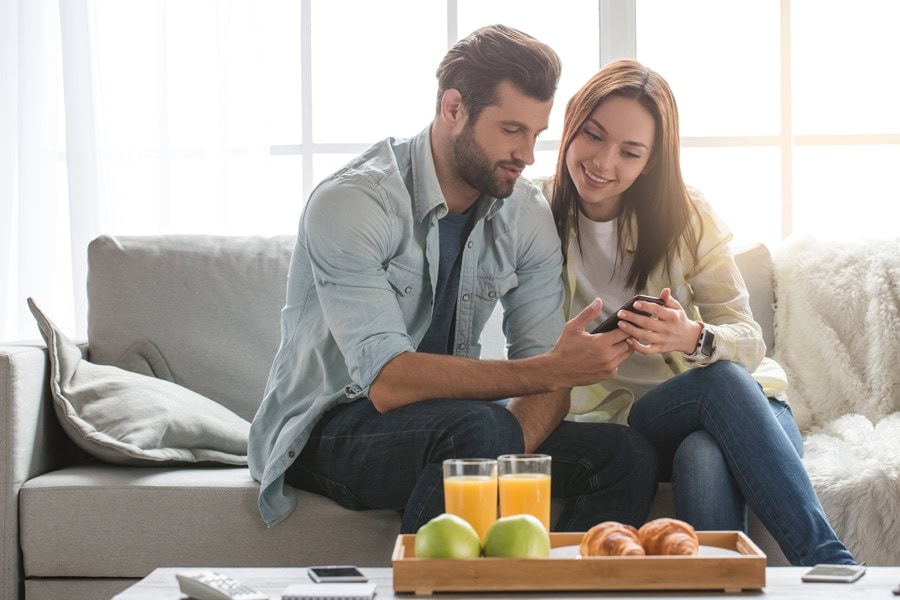 Young woman and man family couple indoors using smartphone.