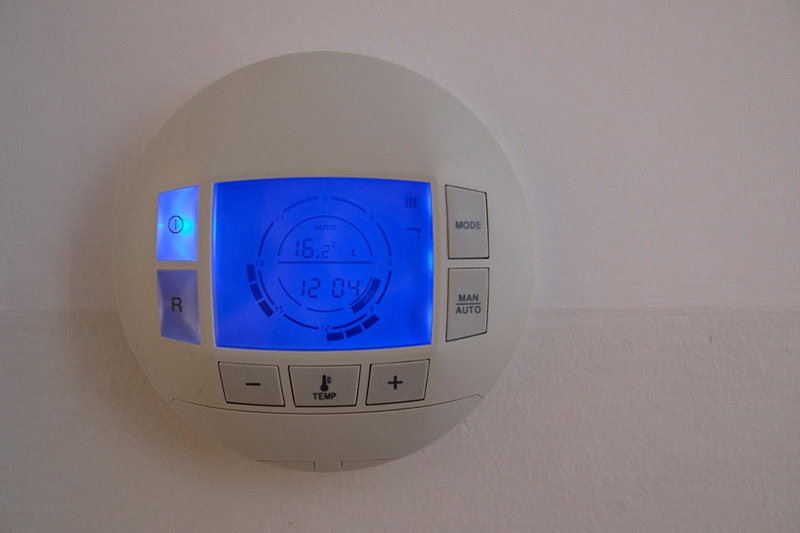 How a Smart Thermostat Can Save You Money During a Heat Wave. Photo of a digital thermostat mounted on a wall.