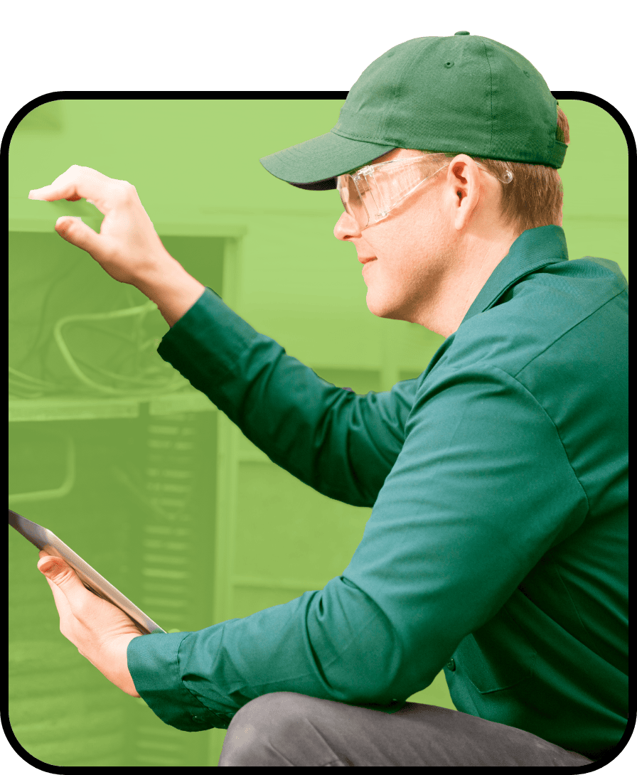 Gagle's Heating technician wearing safety glasses bending down examining equipment, holding a tablet device in one hand.