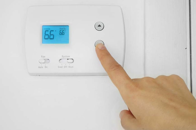 5 Reasons Why Regular HVAC Maintenance is Essential for Marion County Homeowners. Image is a photograph of a person's hand adjusting a wall mounted thermostat temperature.