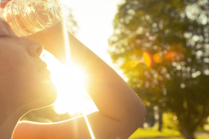 3 Tips to Prevent AC Breakdown During a Heat Wave. Photo of a young woman in the hot sun trying to cool off with a bottle of water.