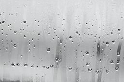 Black and white background of the condensate flowing water on the window glass collecting and flowing down.
